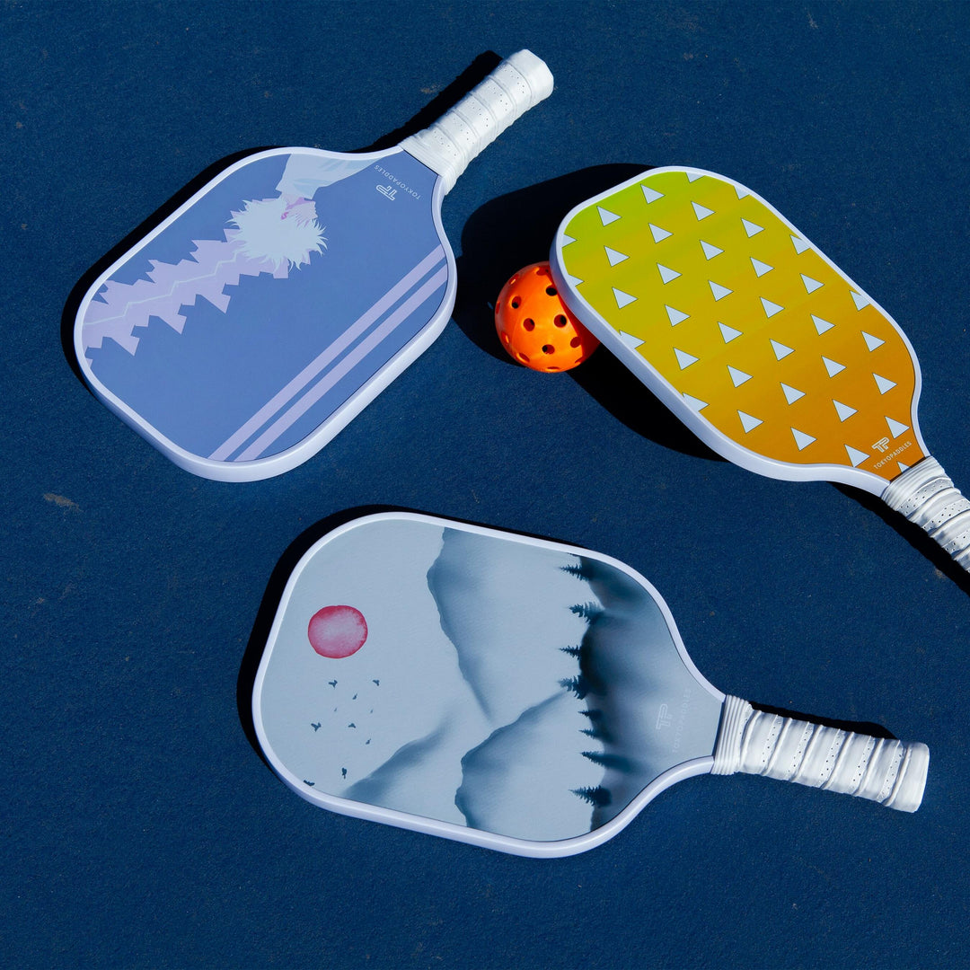 A collection of top-performance pickleball paddles laid out on a soft grass field. Each paddle is designed for silent operation to give a quiet game; reduced noise technology is evident. Materials use